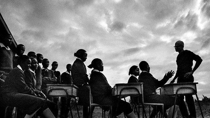 High contrast black and white photo of Microsoft CEO, Satya Nadella, speaking with Kenyan students