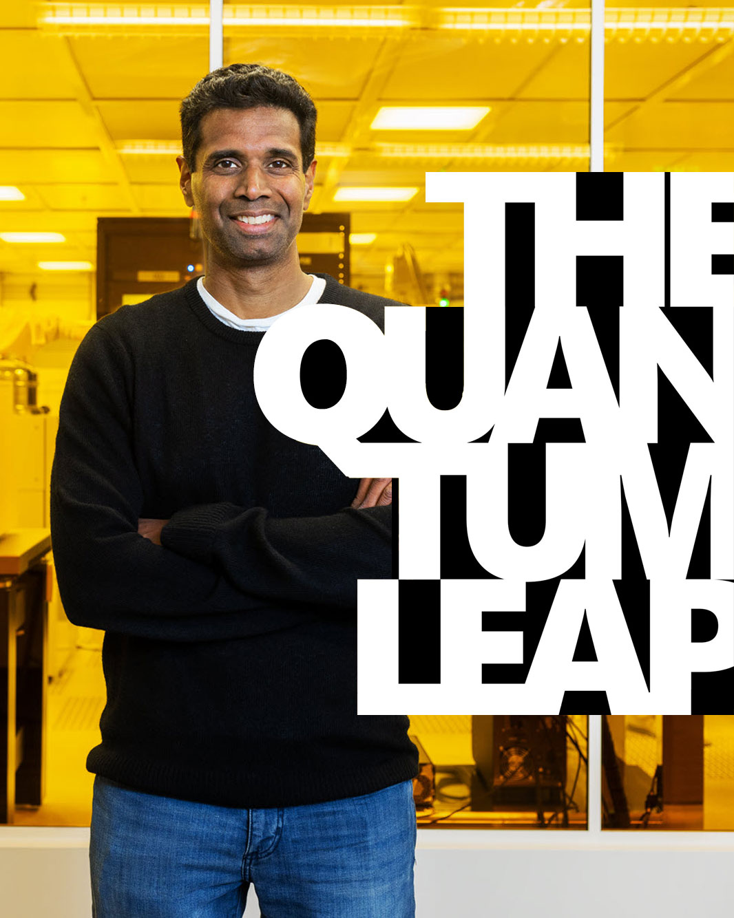 A man in a black sweater and blue jeans stands with arms crossed in a bright, yellow-lit lab. Bold white text partially covers him, reading “THE QUANTUM LEAP.”.