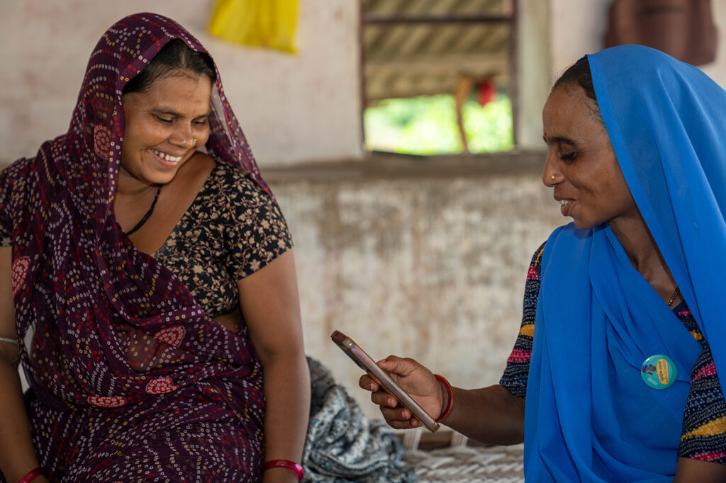 Two indian women in traditional clothing chat. One is holding a phone.