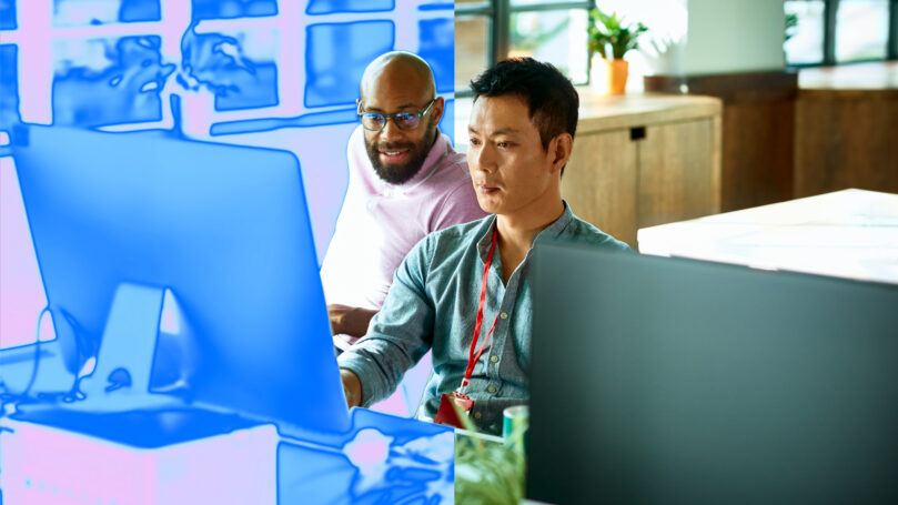 Two colleagues collaborate at a desk, focused on a computer screen with a blue digital overlay in a modern office.