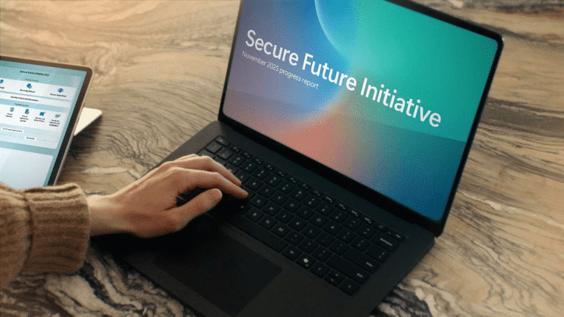 Hand on laptop showing “Secure Future Initiative” progress report screen.