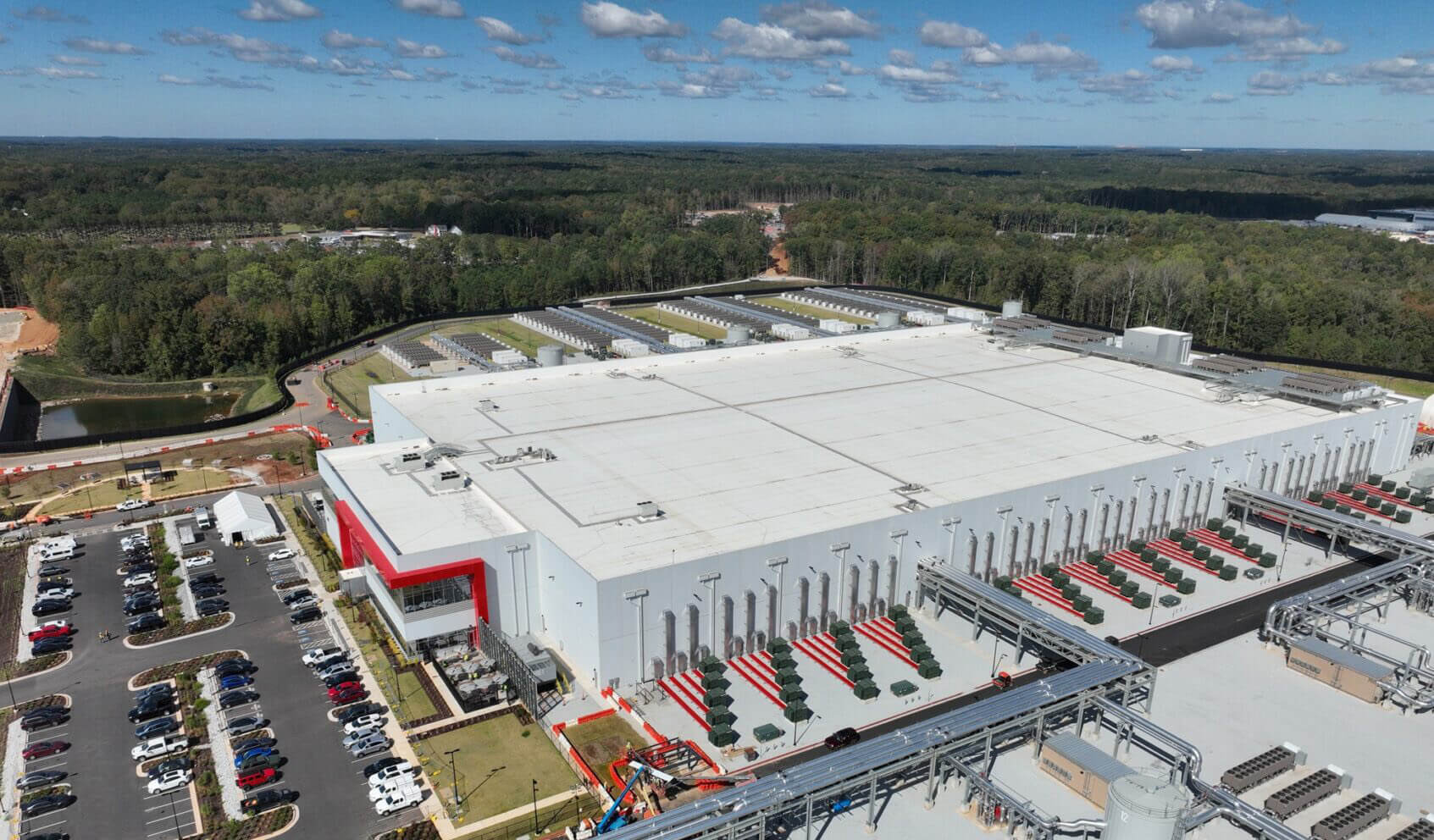 Large industrial datacenter building with parking lot surrounded by forest.
