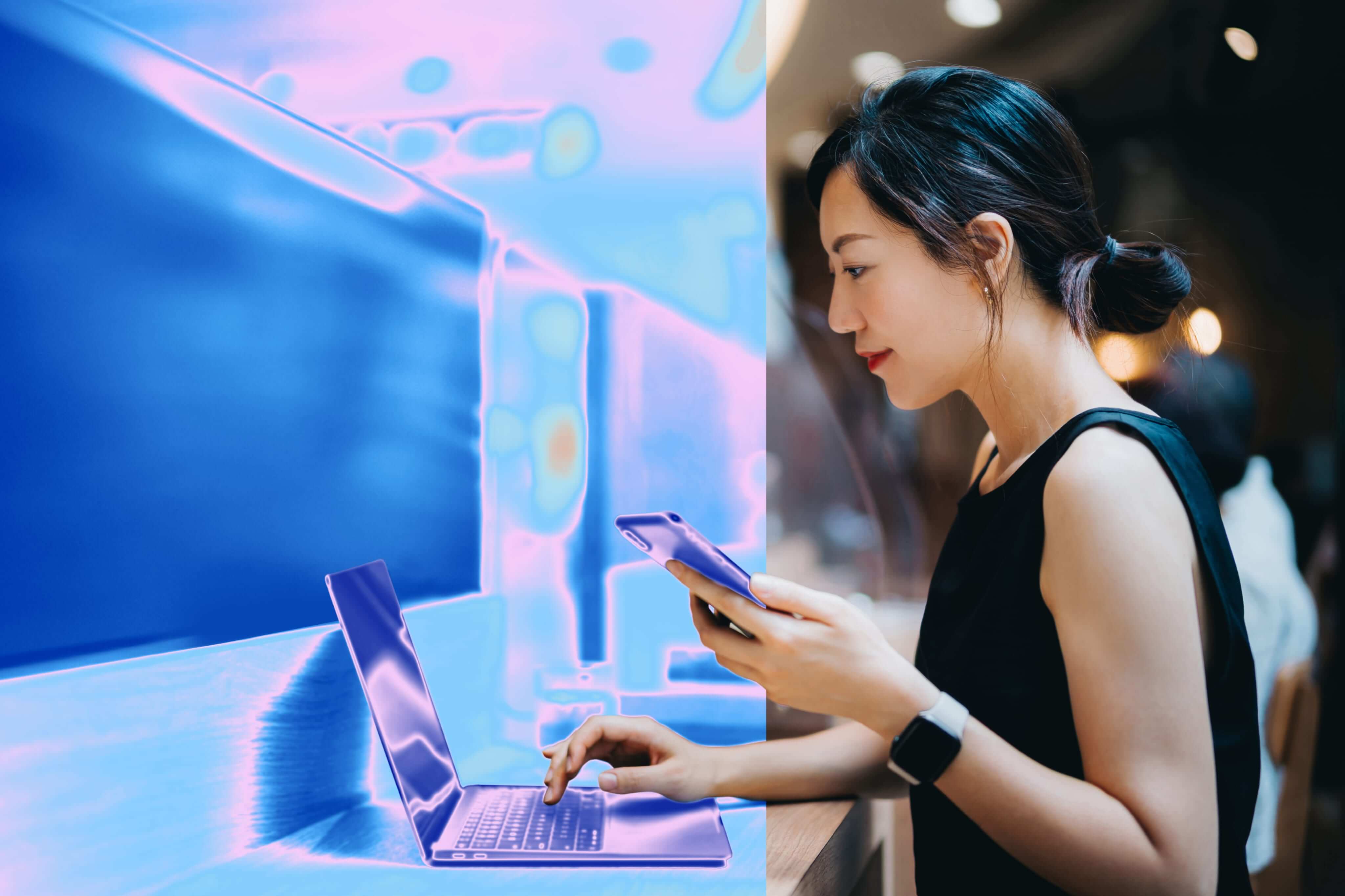 Woman using a laptop and smartphone, shown in thermal imaging colors.