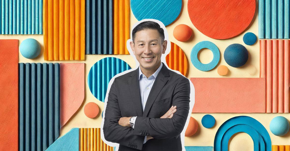 Man in a suit standing with arms crossed against a colorful geometric background of circles, stripes, and arches in blue, orange, and coral tones.