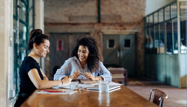 Two people sitting at a wooden table discussing documents in a modern industrial-style workspace