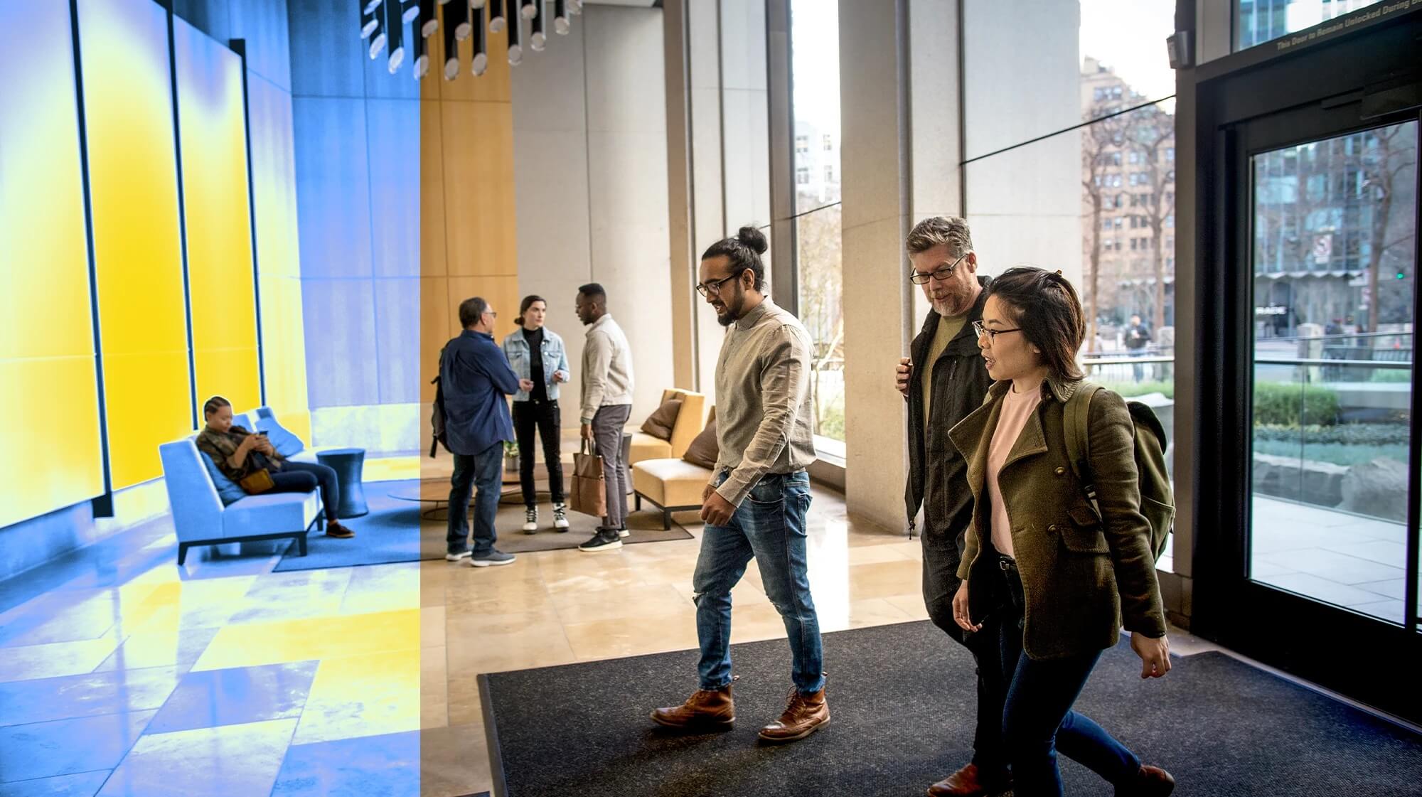 Modern office lobby with a seating area. Several people walking through the entrance while others are chatting near the couches.