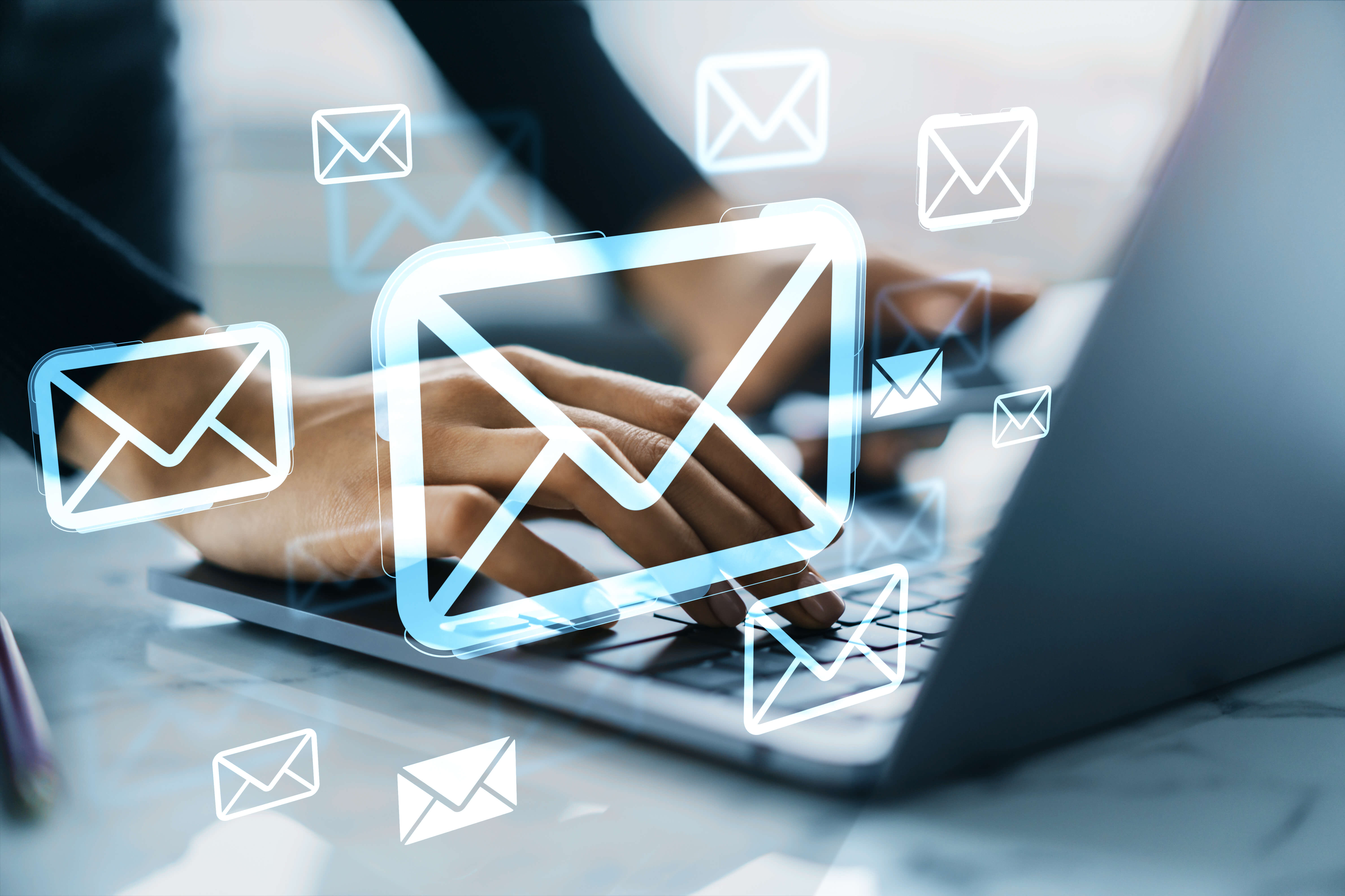 Hands typing on a laptop with glowing email icons floating around.