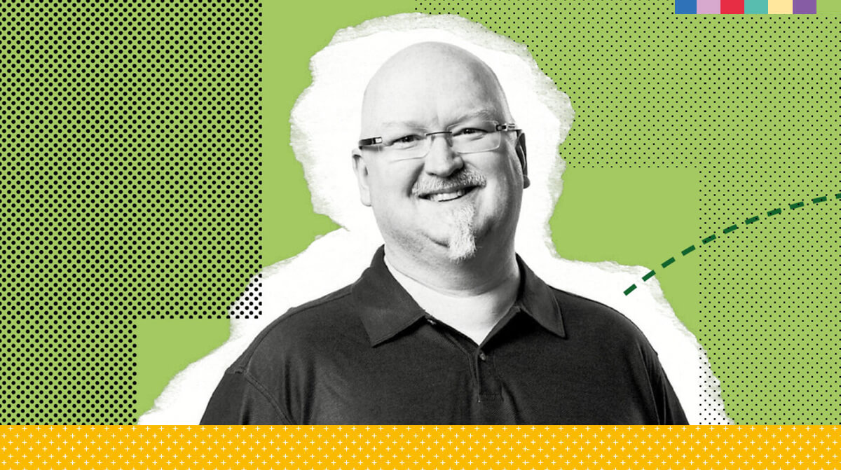 Man wearing a dark collared shirt against a green patterned background.