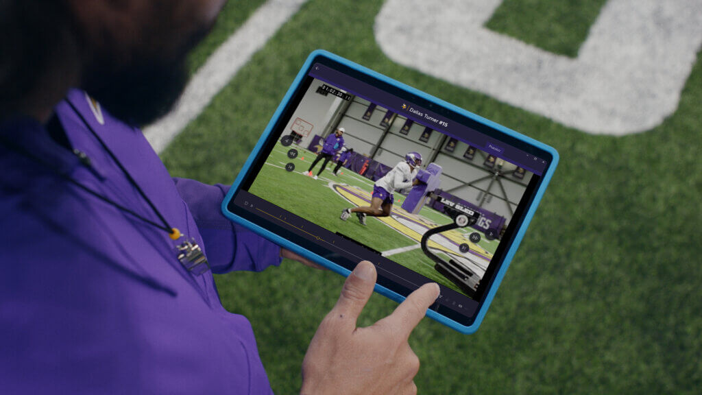 a coach holding a tablet showing a football practice video on a field