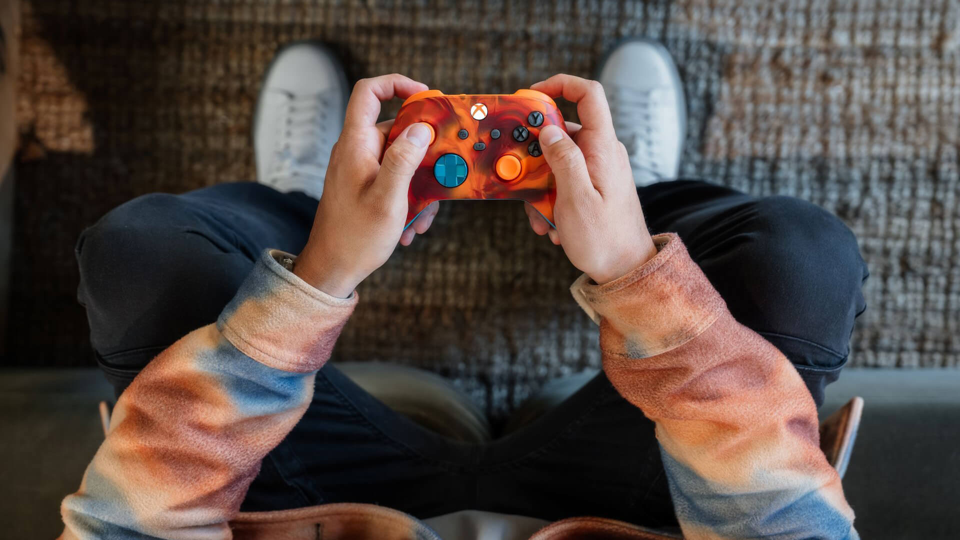 Person holding an orange game controller while sitting on a couch.