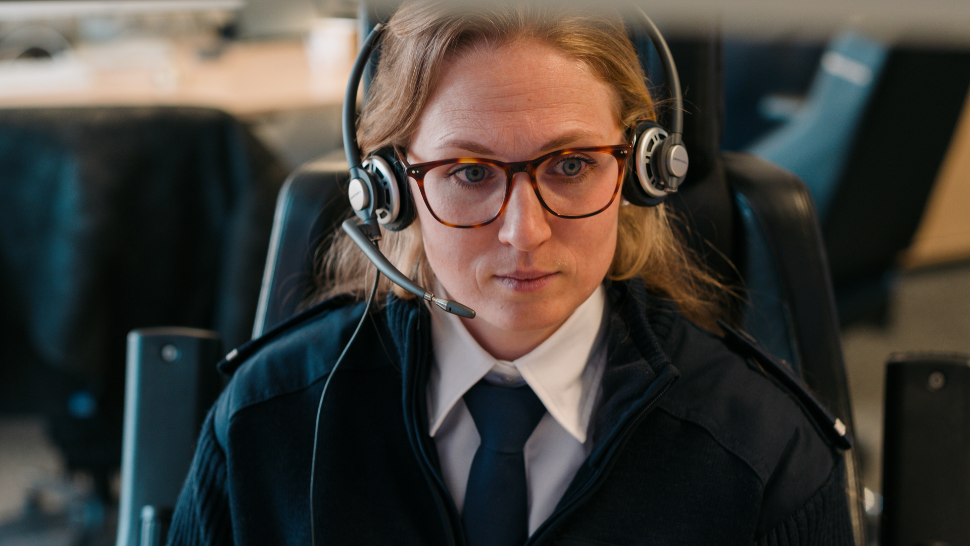 Emergency dispatcher wearing a headset, seated at a control console.