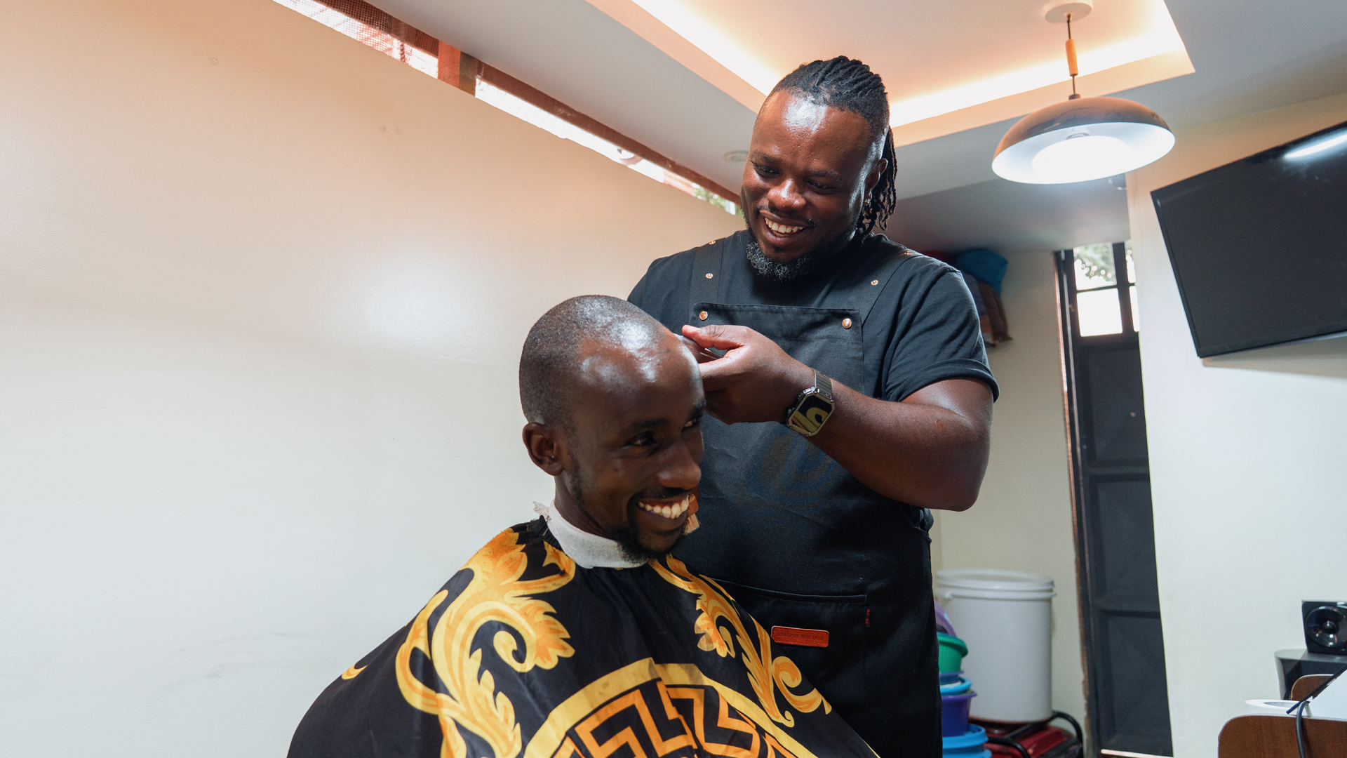 A barber trims a client’s hair inside a small, well-lit salon.