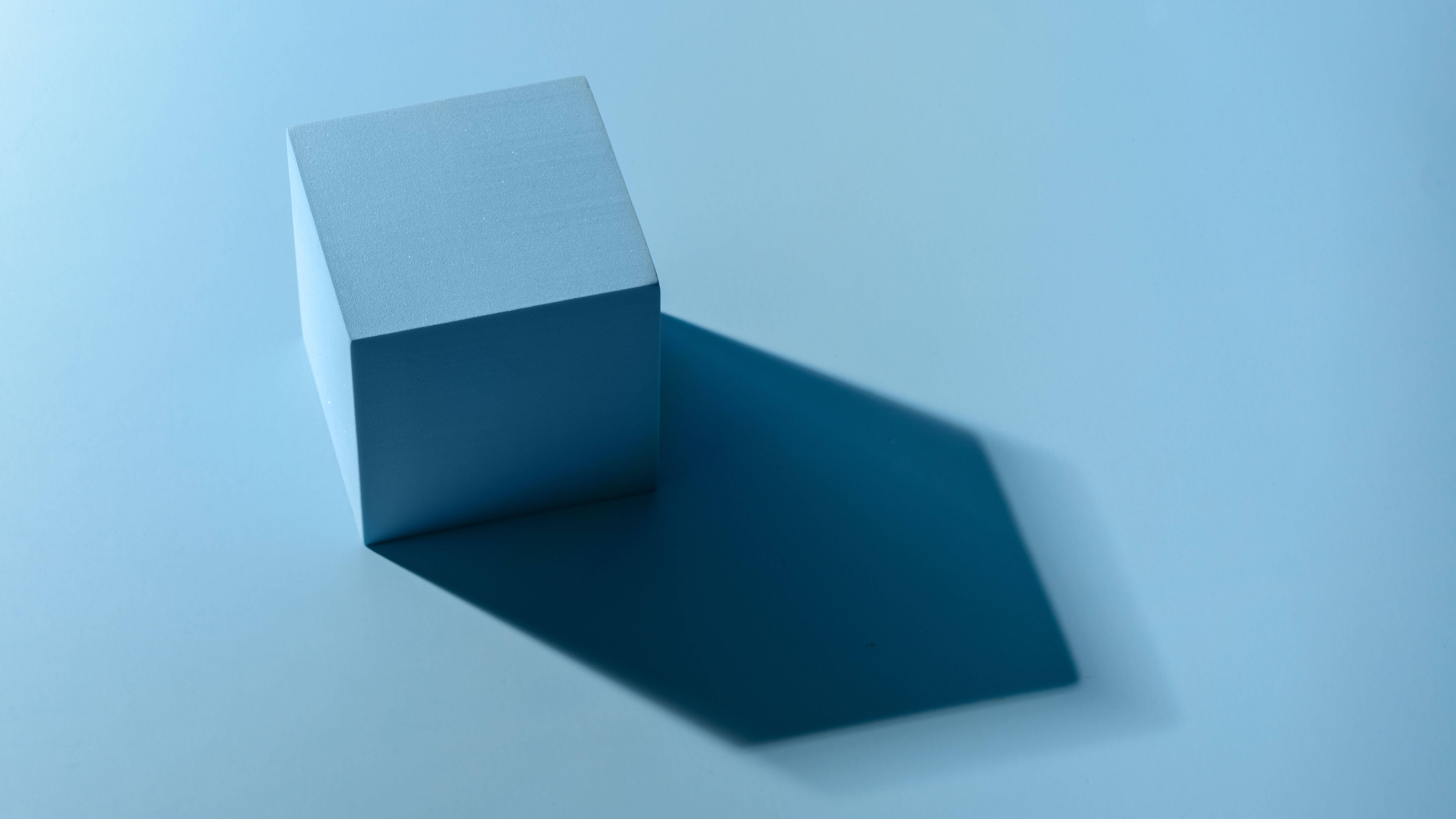 A light blue cube casting a long shadow on a blue surface.