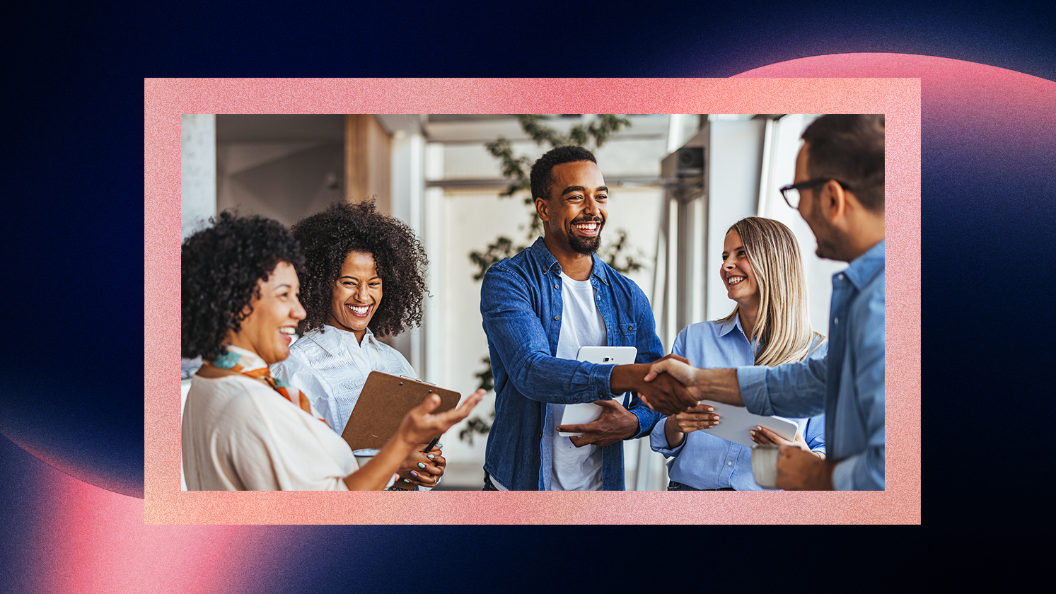 A group of colleagues standing indoors, talking and shaking hands during a meeting.