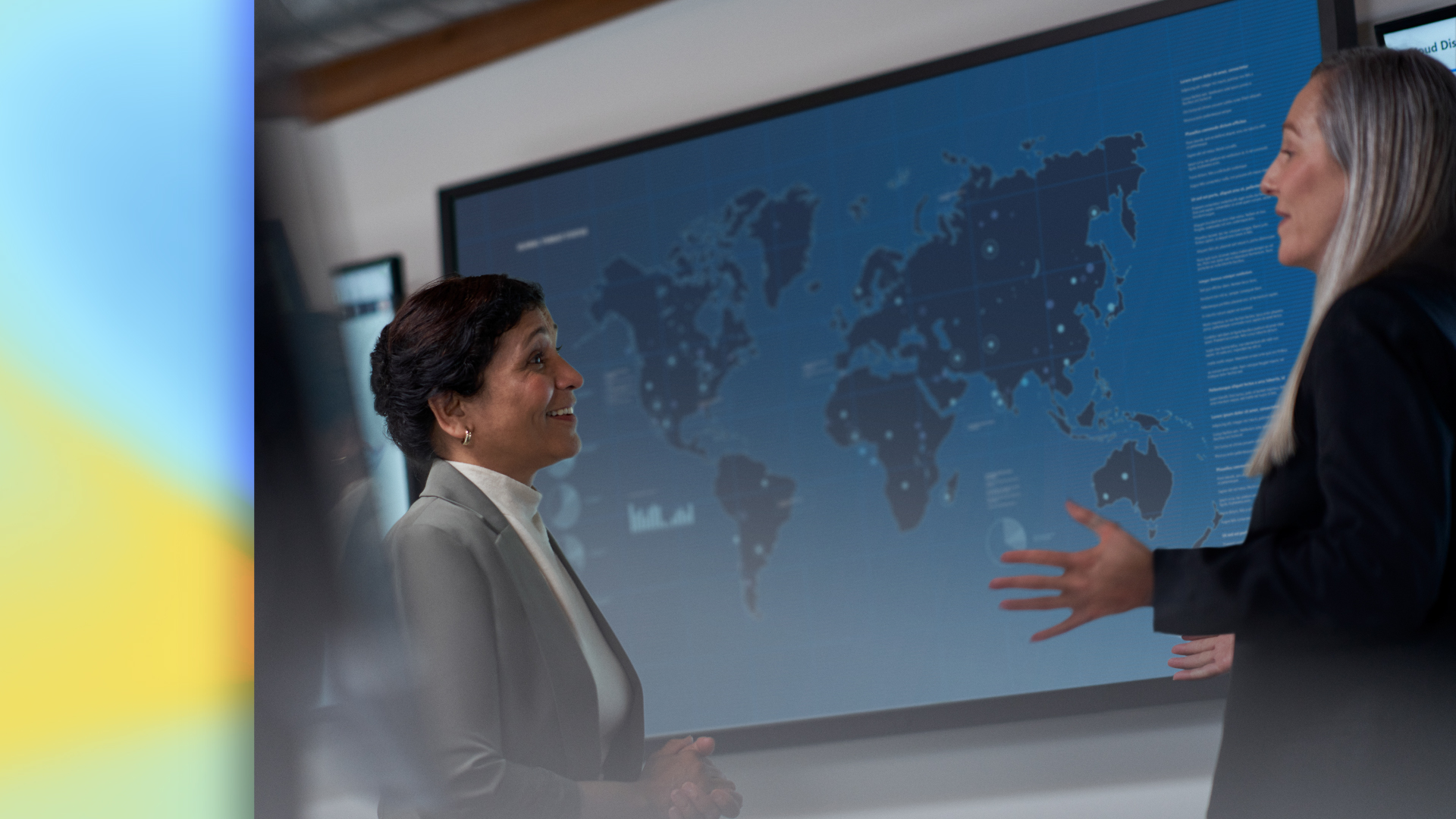 Two people discuss data in front of a large digital world map display.