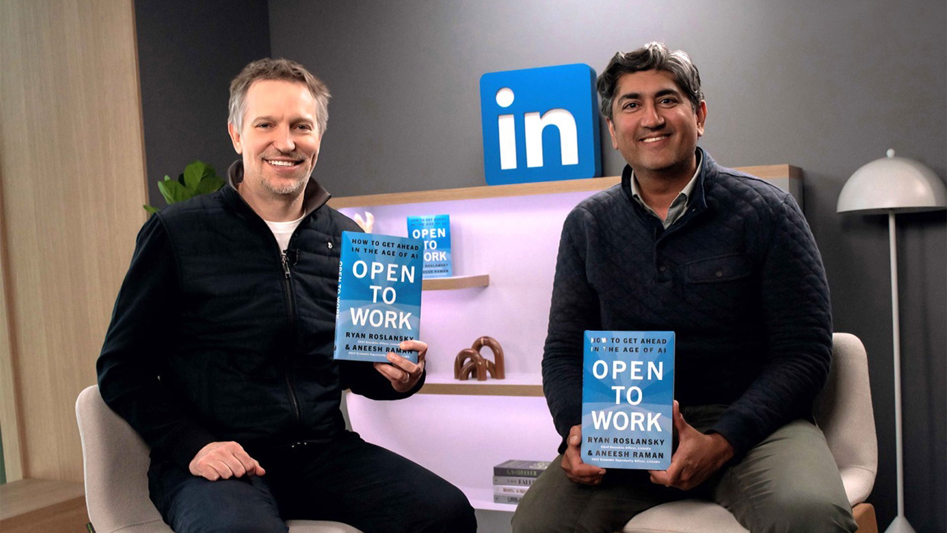 Two men seated, smiling and holding copies of the book Open to Work, with a LinkedIn logo behind them.