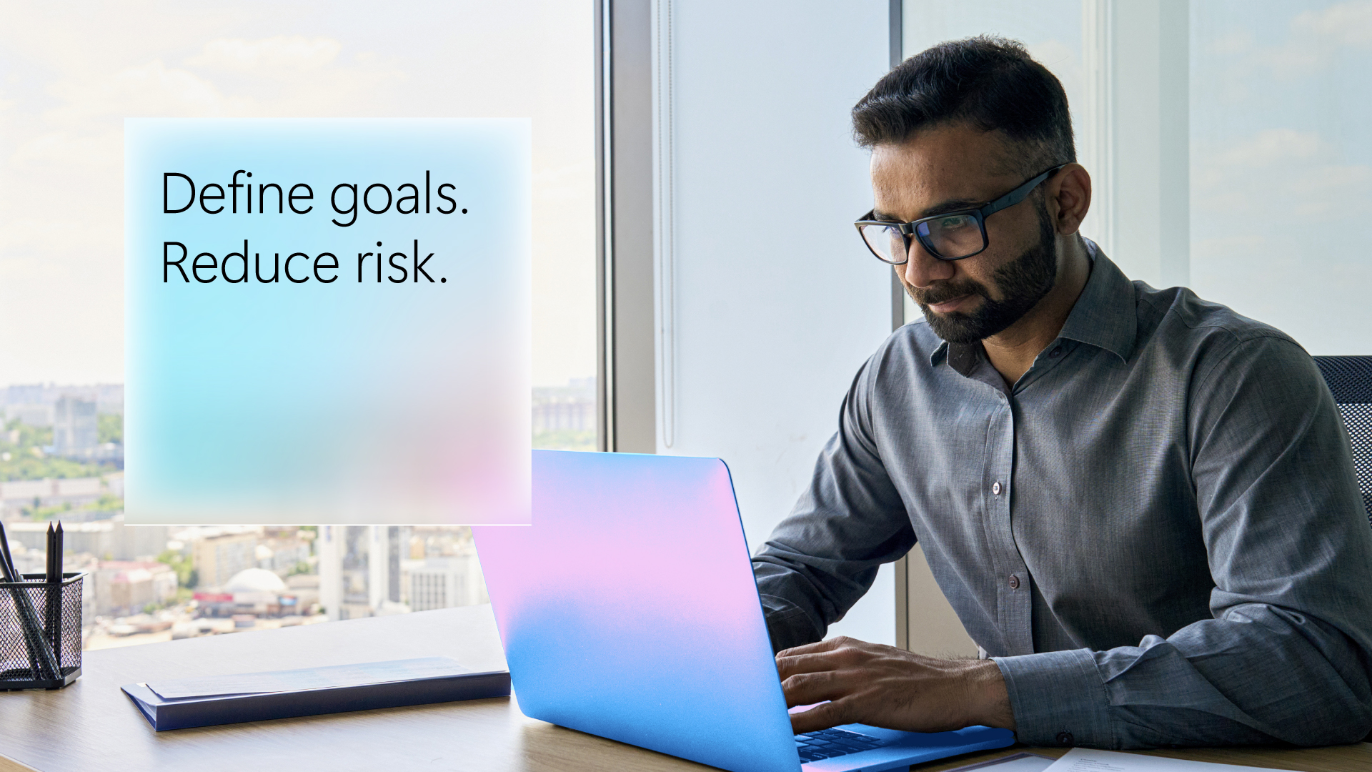 Man working on a laptop at a desk, with text reading “Define goals. Reduce risk.”