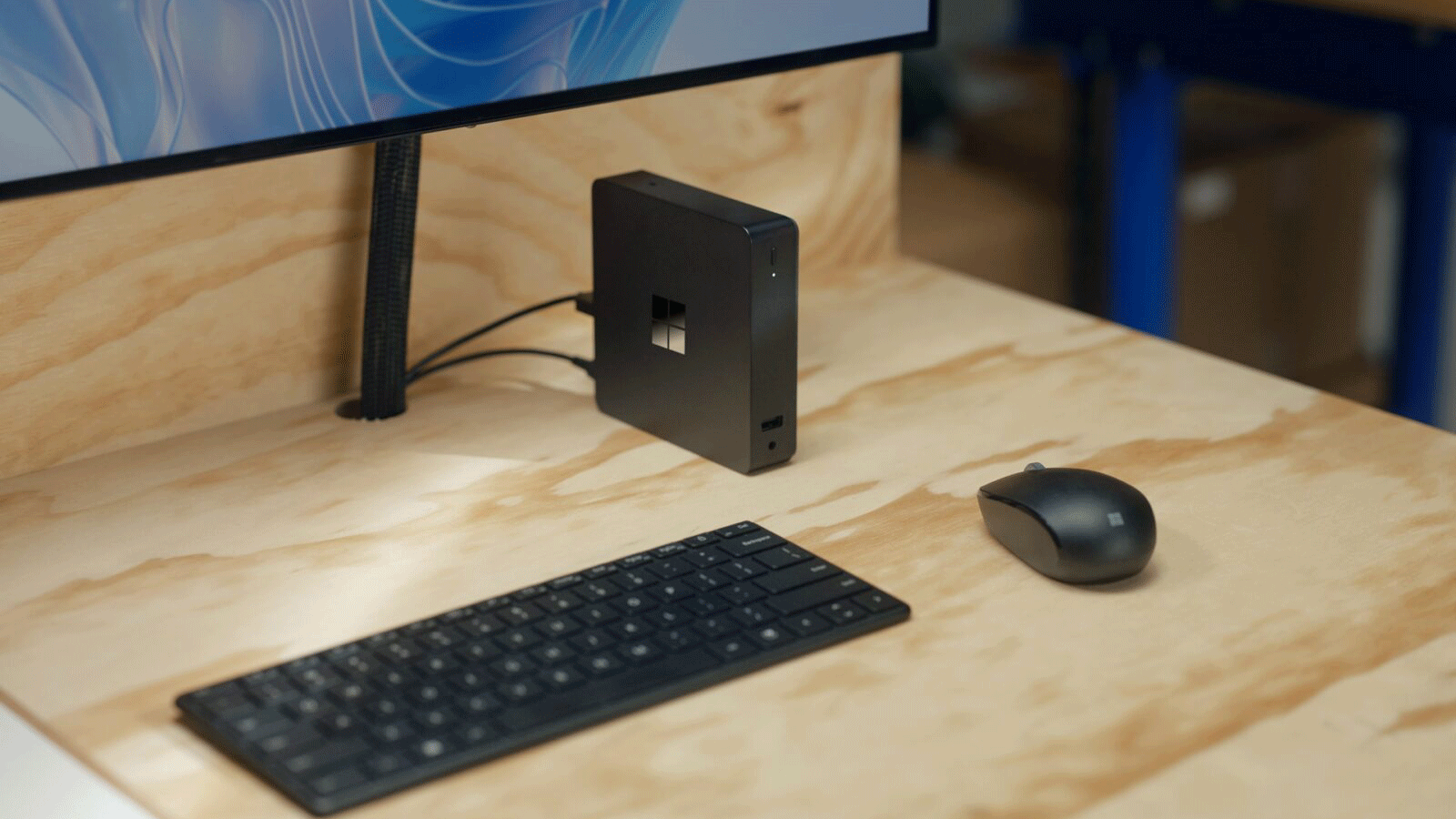 Microsoft's Windows 365 Link device on a wooden desk beside a keyboard, mouse and monitor.