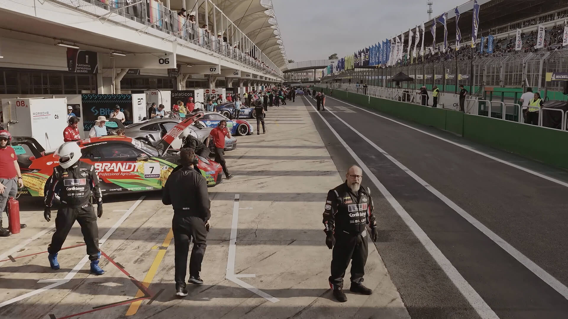Race cars lined up in a pit lane with crews and drivers preparing.