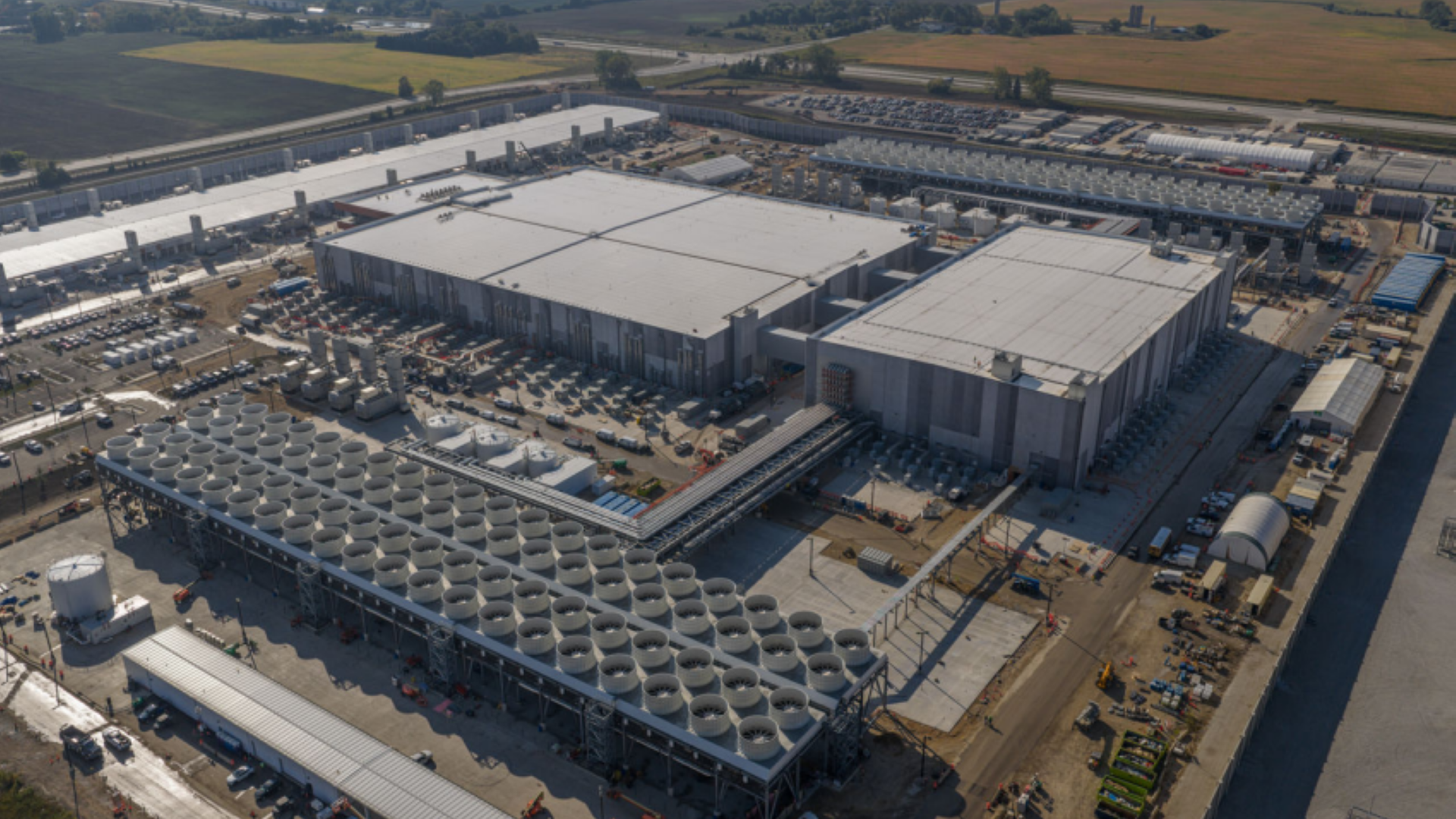 Aerial view of a large data center complex with rows of cooling units and surrounding farmland