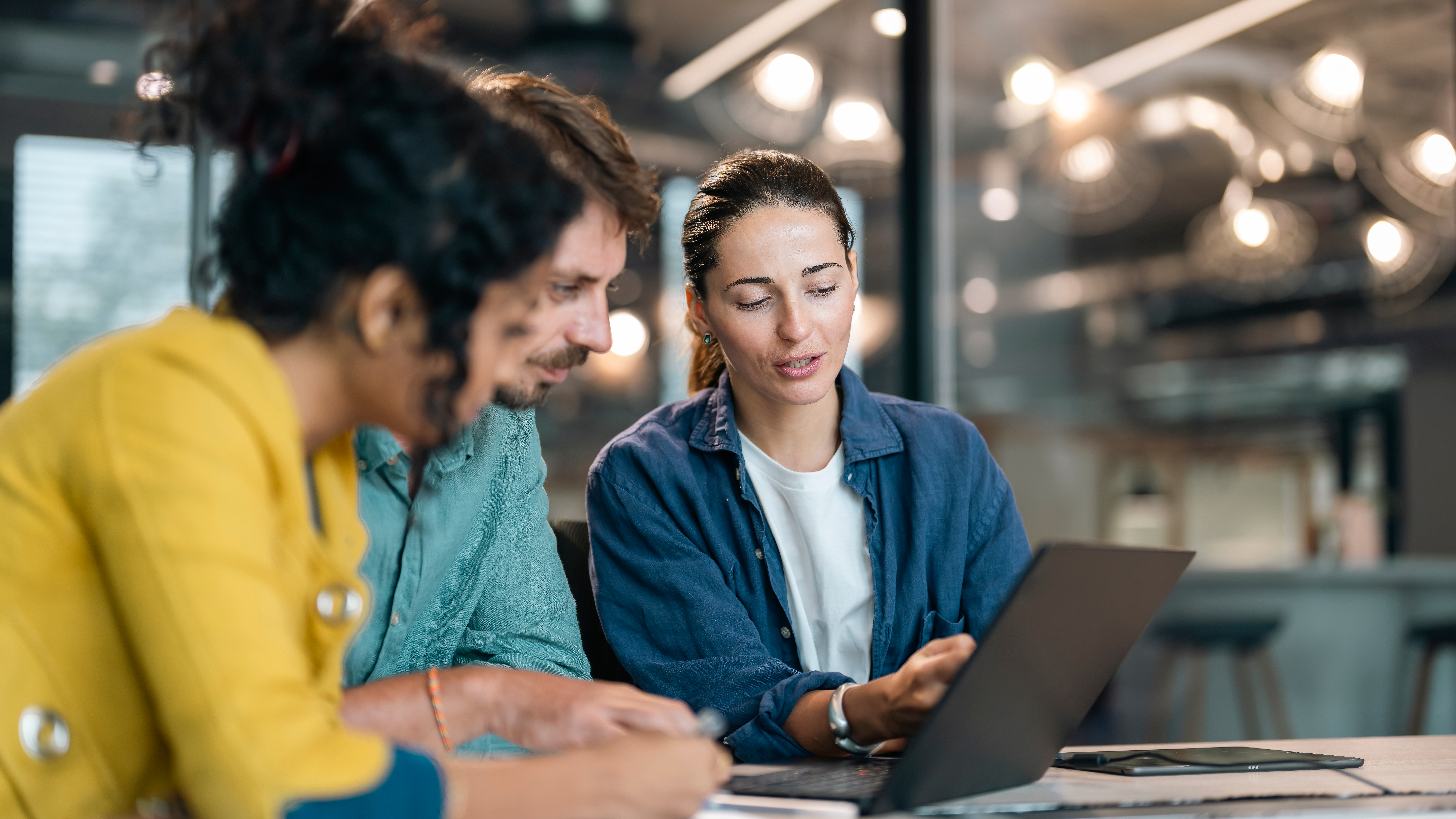 Three people collaborate at a table, reviewing a laptop together.