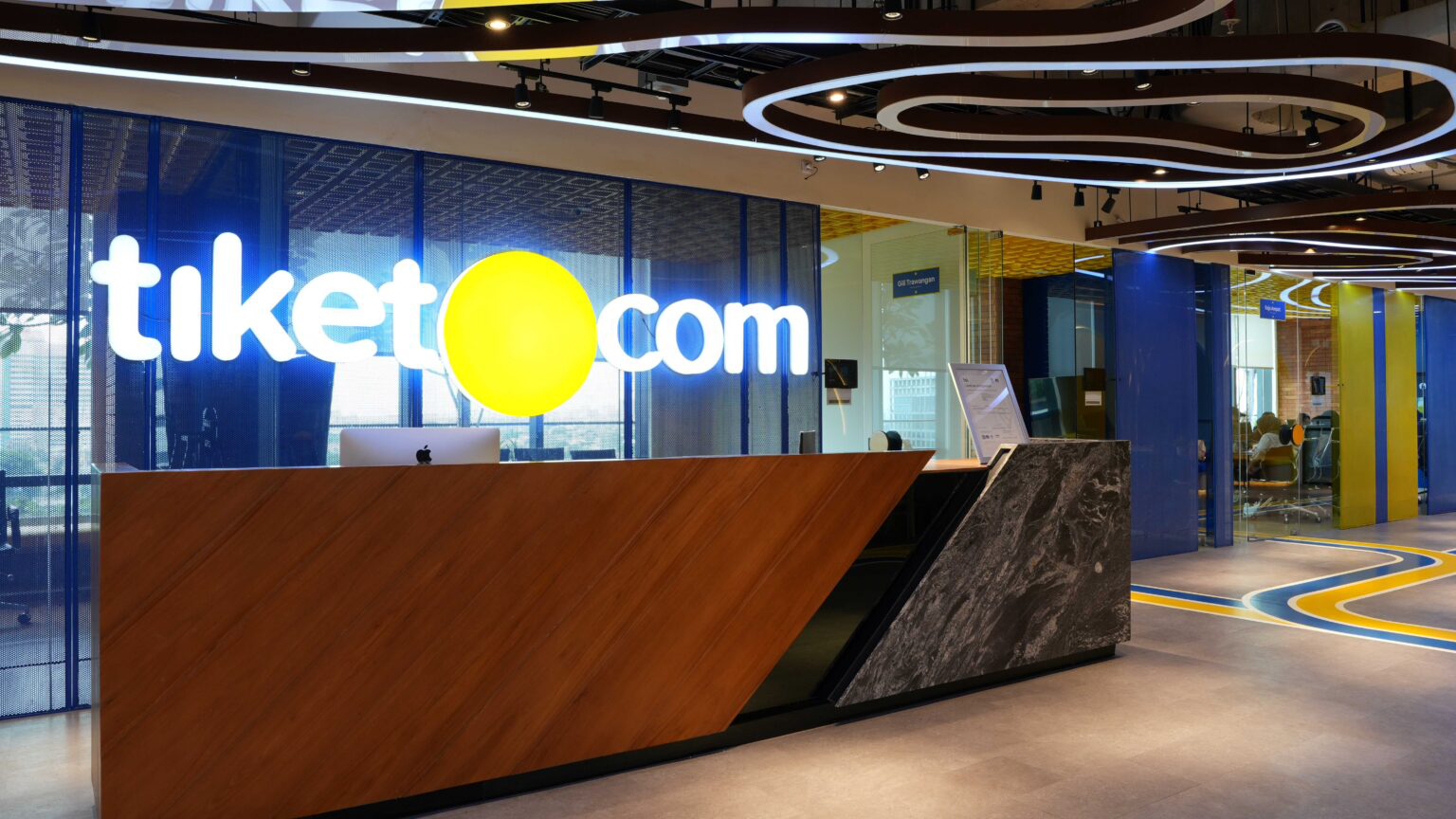 Modern office reception area with illuminated tiket.com logo and curved ceiling lights.