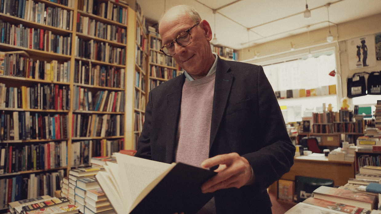 Person browsing a book in a bookstore lined with tall bookshelves.