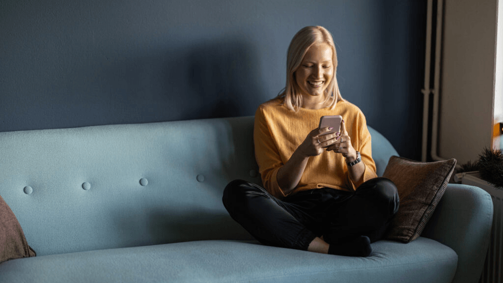 Person sitting cross-legged on a couch, looking at a smartphone.