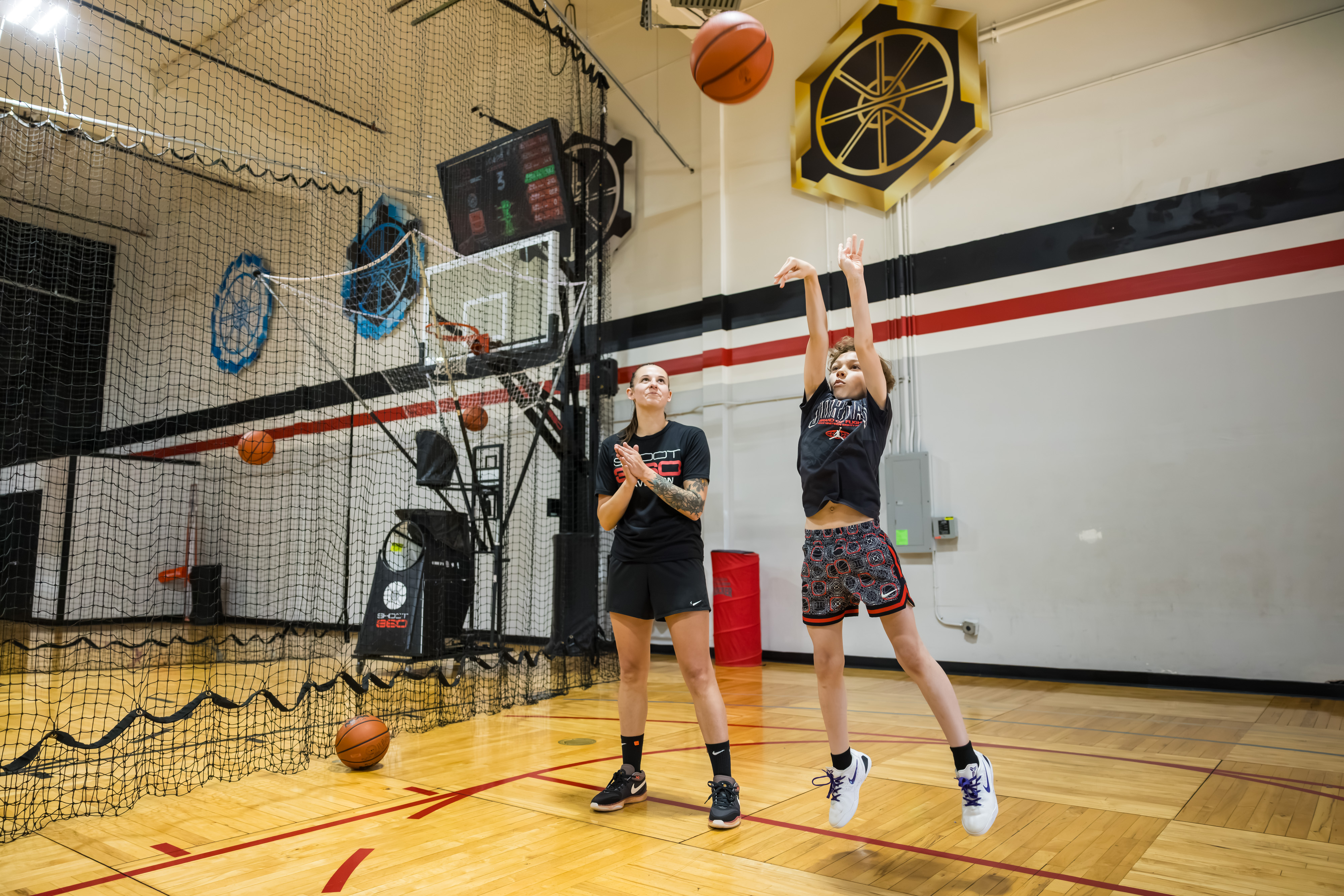 Copilot said: Basketball player takes a jump shot during practice while a coach watches.