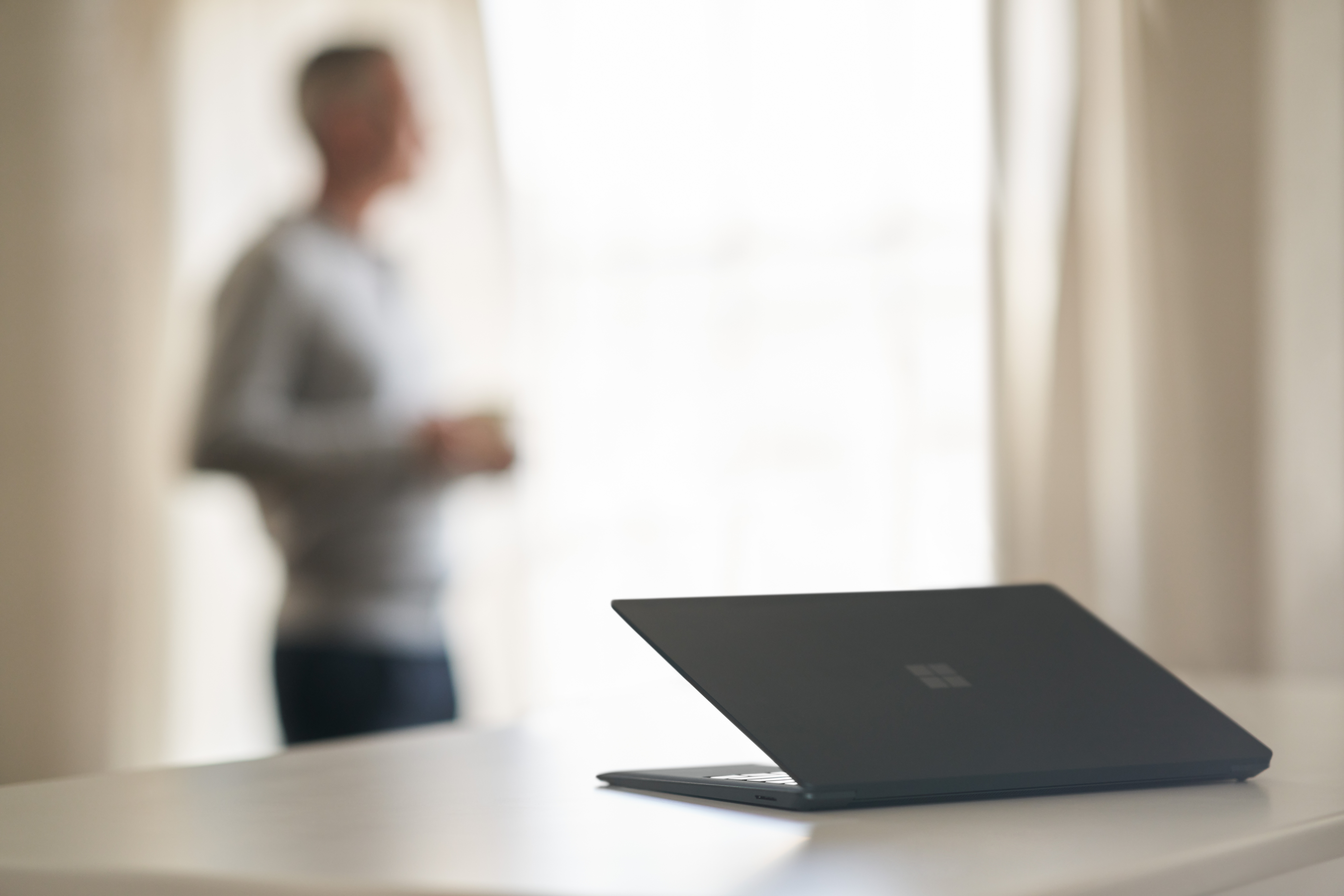 Open laptop on a desk with a person standing blurred in the background.