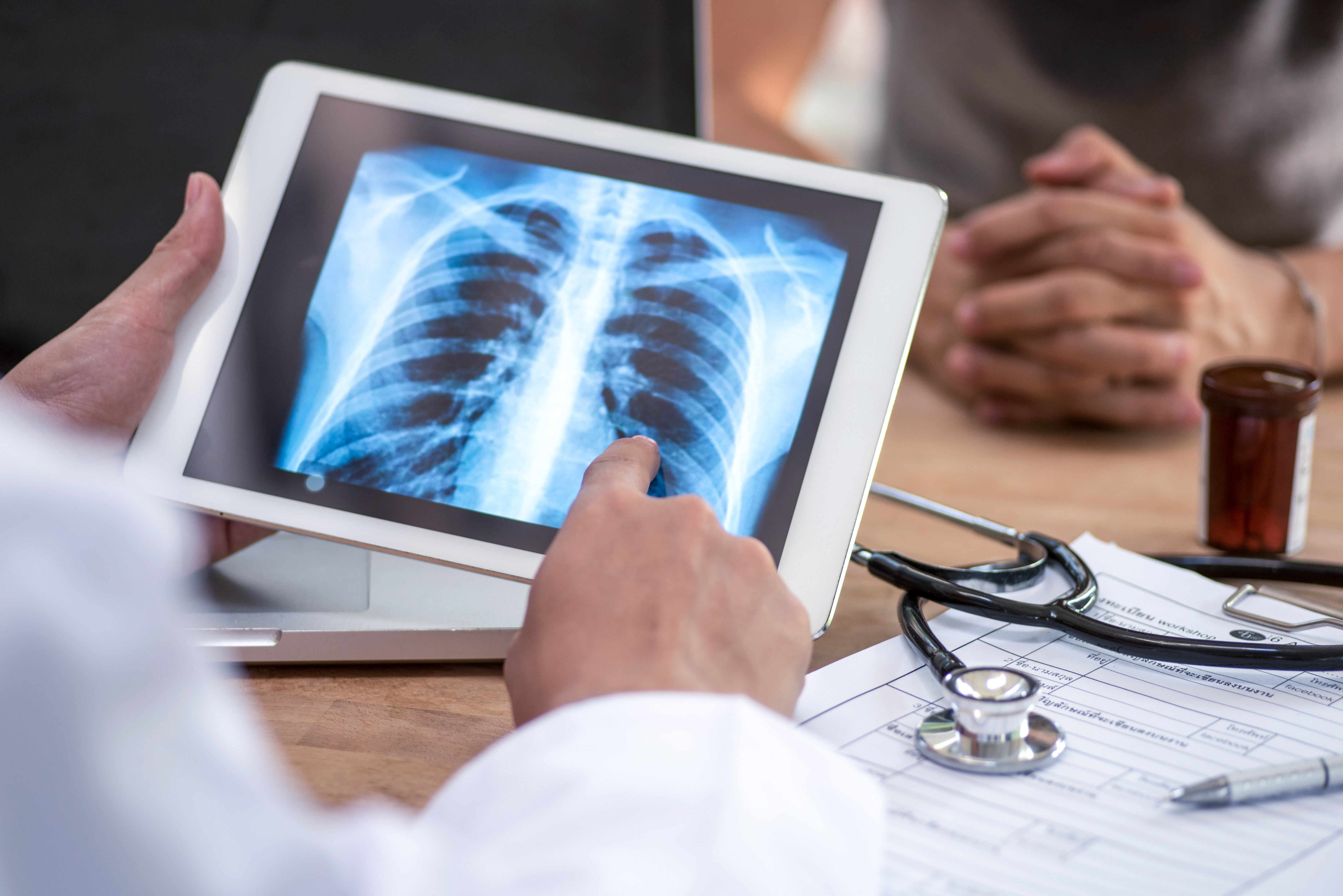 Doctor reviews a chest X-ray on a tablet during a patient consultation.
