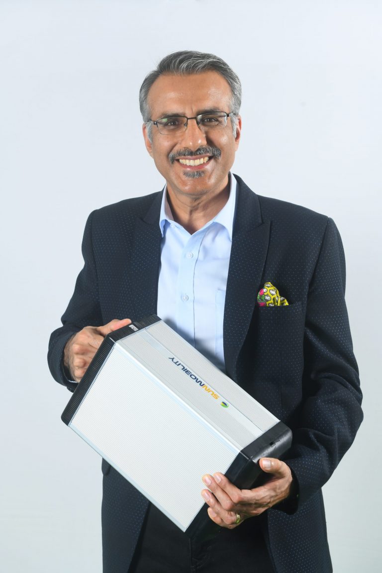 a man looking a the camera and smiling while holding a battery