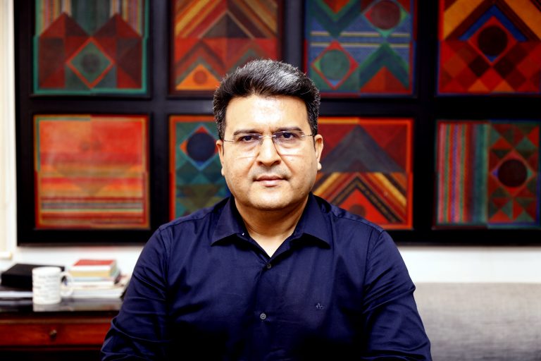 Portrait photo of a spectacled man sitting in his office with colorful abstract art in the background