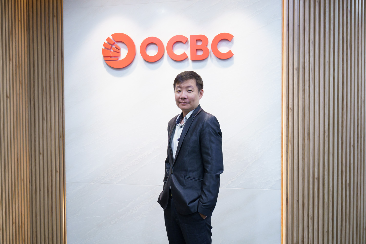 Portrait of a man standing in front of a red OCBC logo
