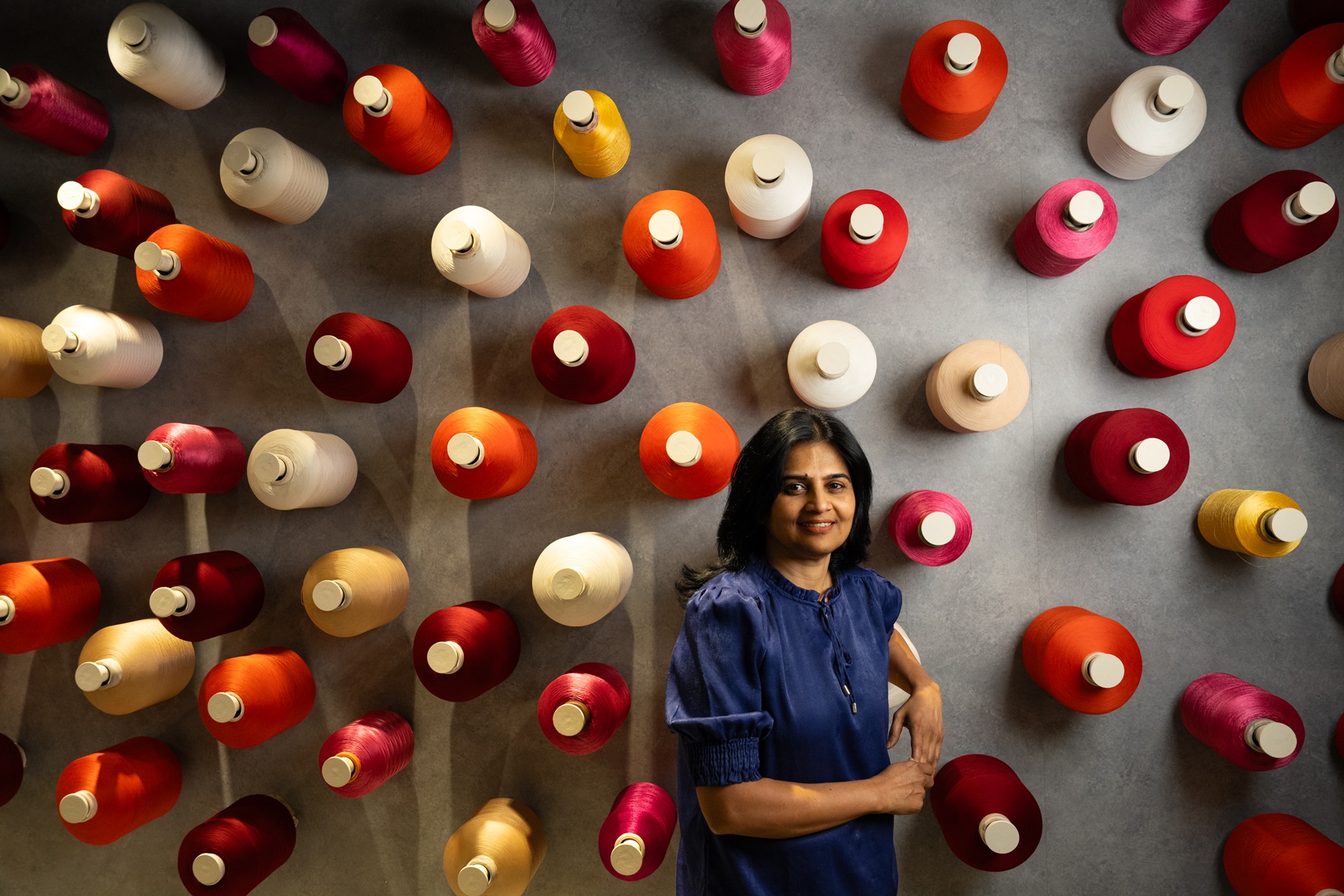 Portrait photo of a woman standing in front of a wall of oversized colorful spools of thread