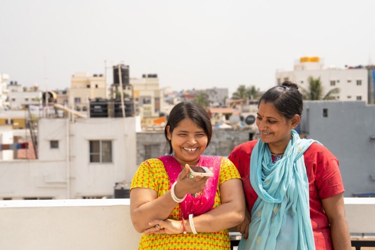 Two women resting against a parapet speaking into a smartphone