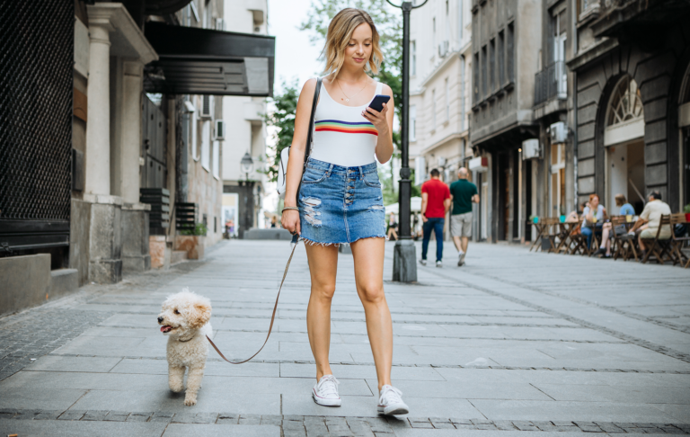 Woman walking her dog on a pavement while looking at her phone