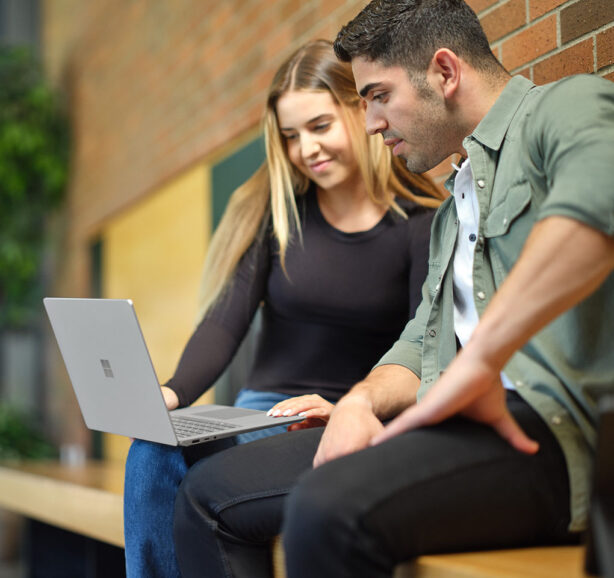Two people sitting next to each other looking at a laptop