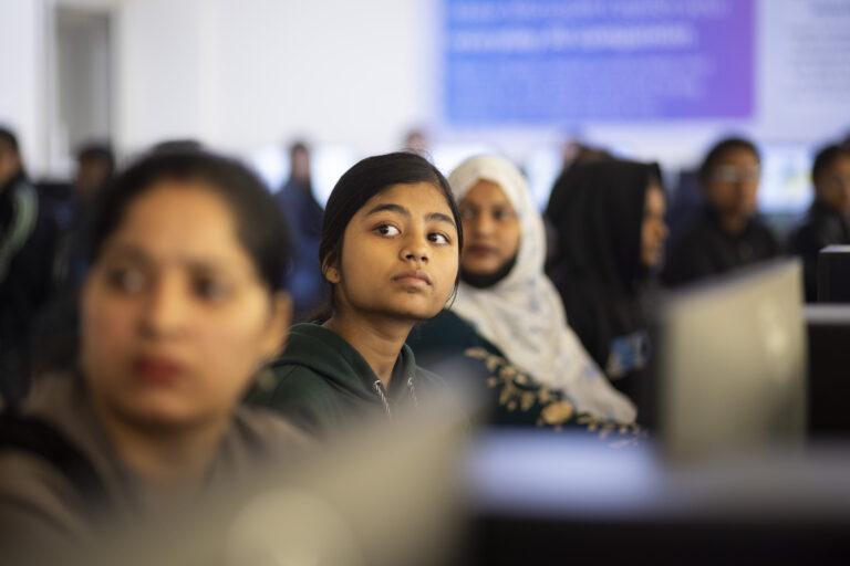 A group of young women look up from their computer screens.