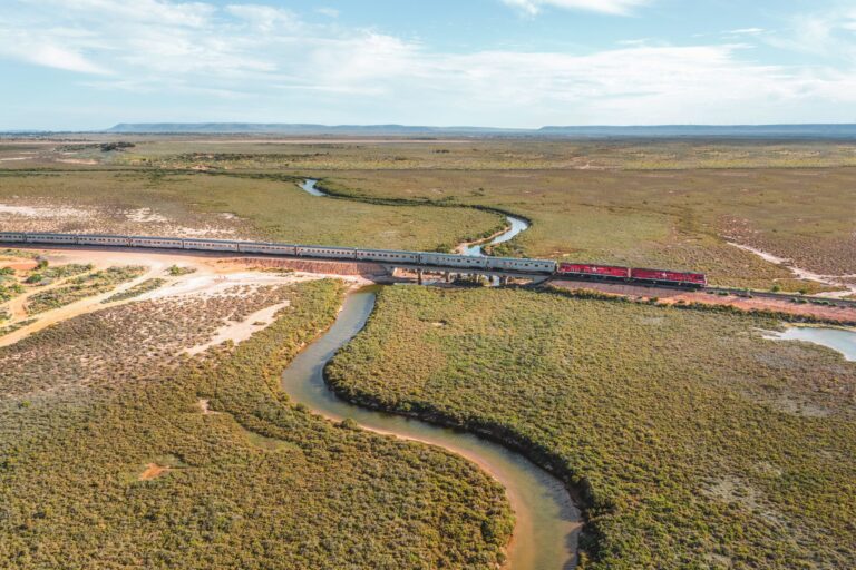 Aerial shot of a train running through a scene of greenery and a river