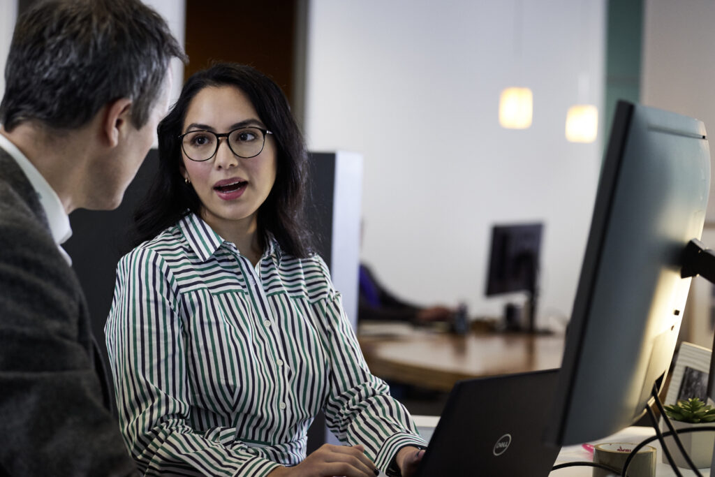 Image of two people talking in front of a computer. 