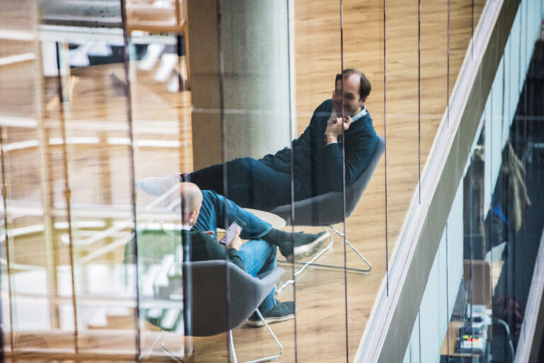 Image of the reflection of two people sitting in chairs in an office building talking.