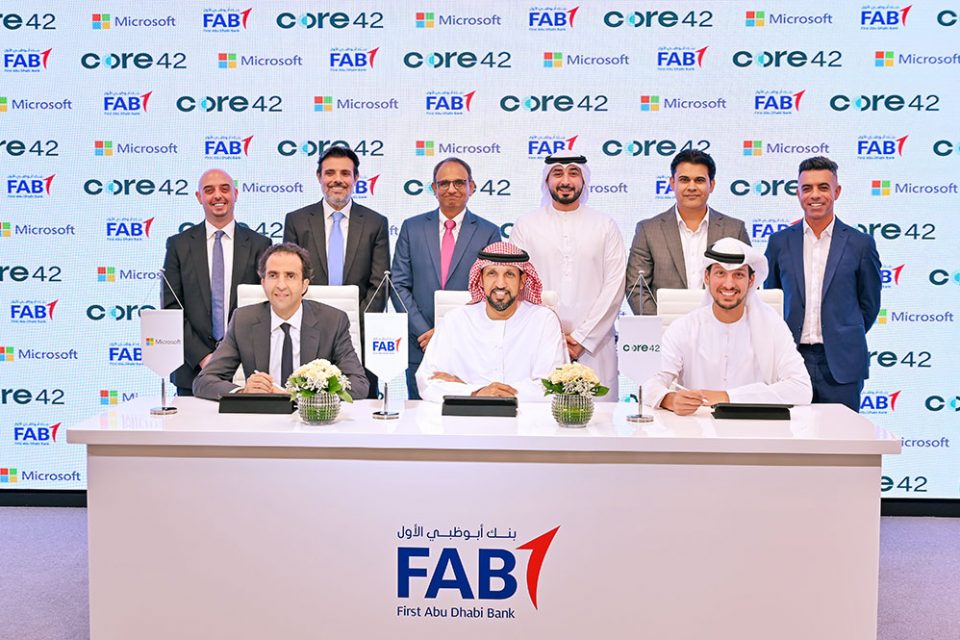 Group of men in Western and traditional Emirati dress assembled for a group picture in front of a wall showing corporate logos