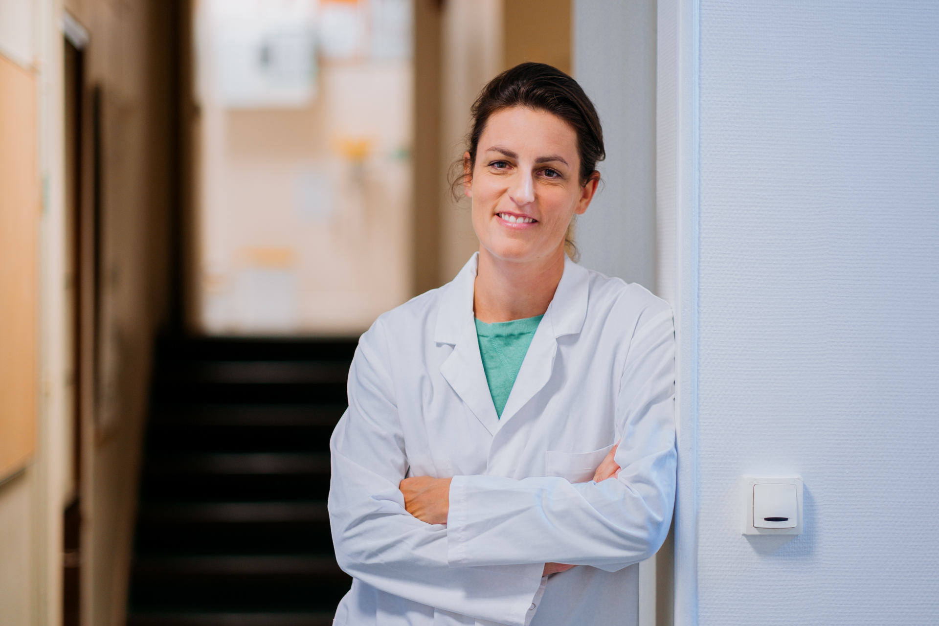 A woman in a white lab coat stands in a doorway.