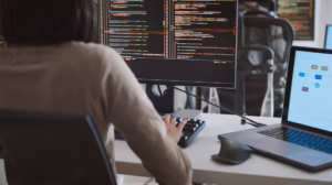 Una mujer de espaldas trabajando en un ordenador. Fondo de pantalla negro y líneas de texto.