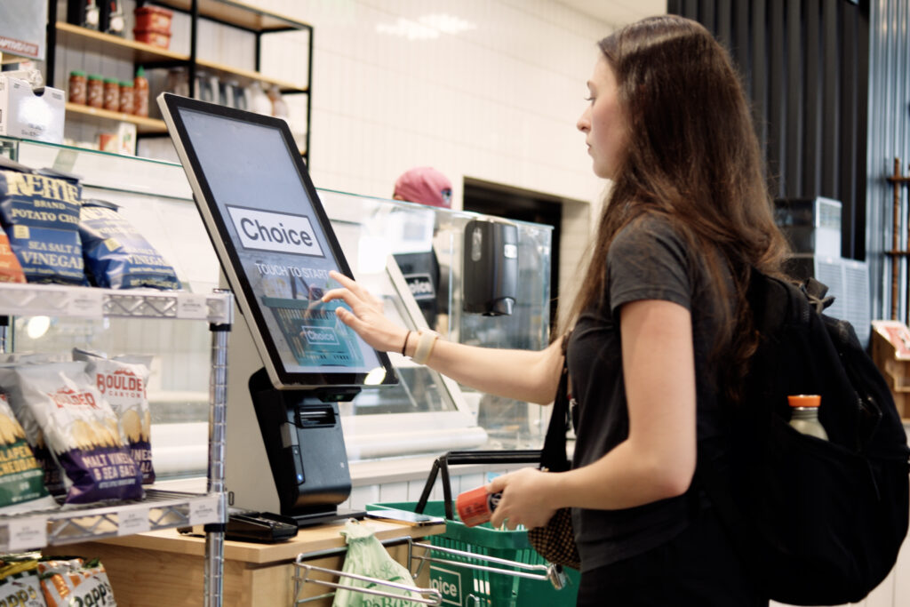 Una mujer joven se registra en una computadora con pantalla táctil en una tienda de conveniencia Choice Market en Denver.
