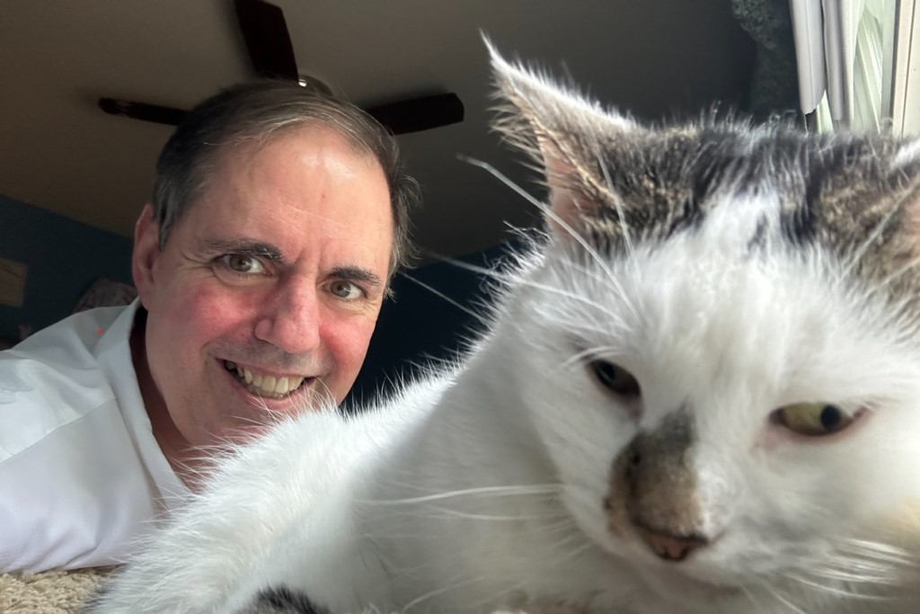 Jim DeMarco mira con una sonrisa detrás de su gato, el Sr. Darcy.