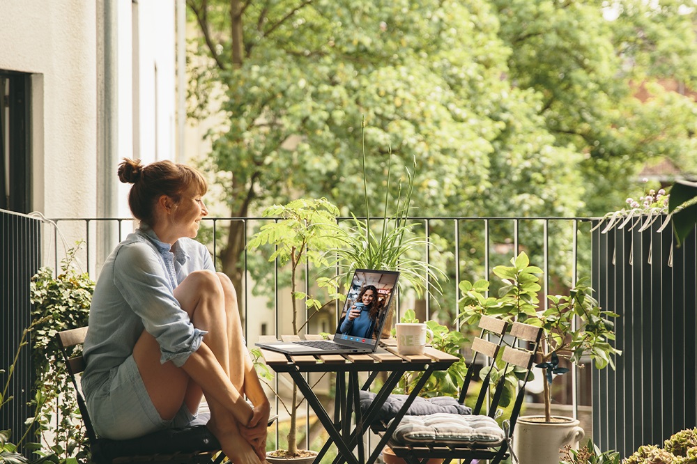 Mujer sentada en una mesa en un patio al aire libre participa en una videollamada con computadora portátil sobre la mesa