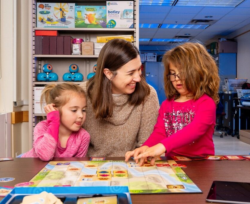 Una mujer que sonríe y dos niñas, juegan en un aula
