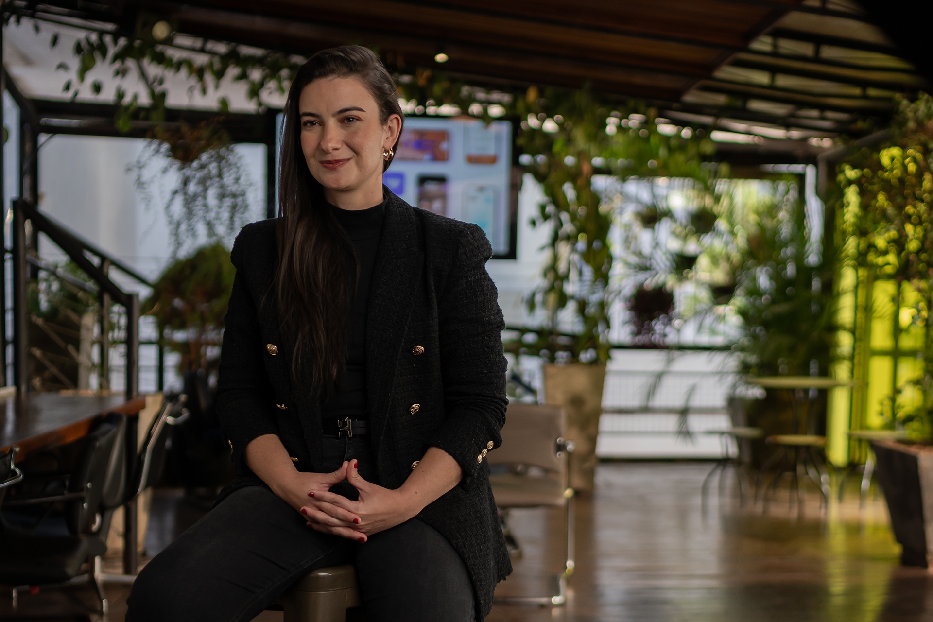 Una mujer está sentada en un taburete, sonriendo con las manos entrelazadas 